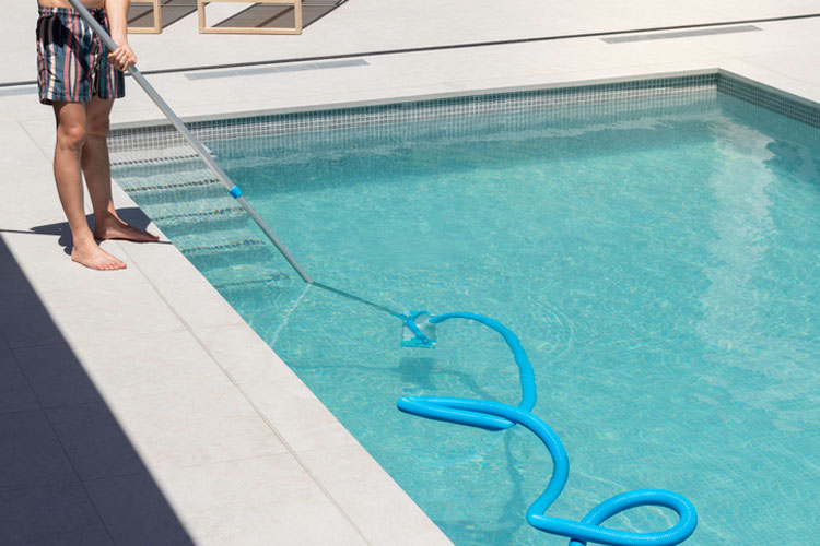 Eine Person reinigt den Poolboden mit einem manuellen Bodensauger und einem blauen Reinigungsschlauch in einem privaten Pool.